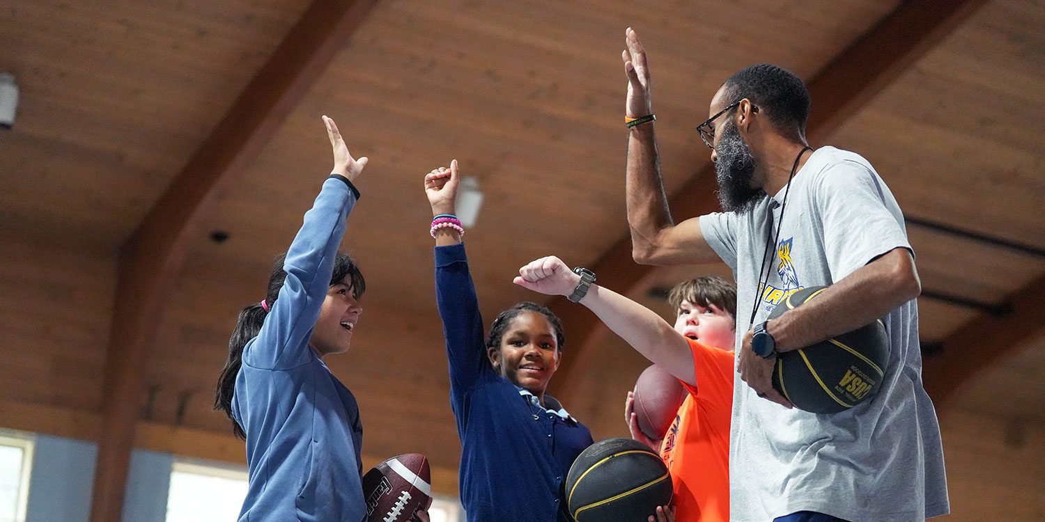 On the basketball court, the basketball coach and some students exchange high-fives.